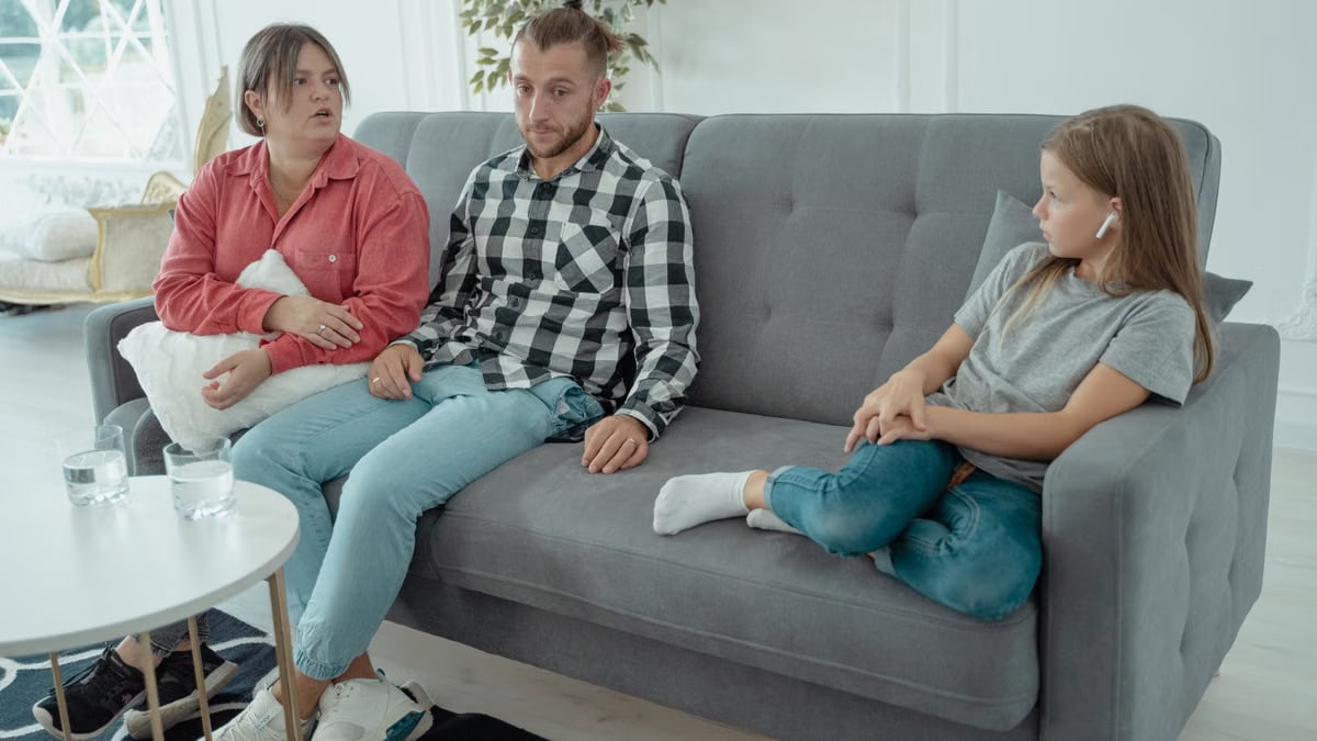 A family sits together on a sofa, discussing in a comfortable home setting, indicating a counseling session.